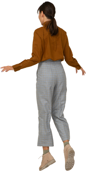 Vista posterior de tres cuartos de una joven asiática saltando en calzones y blusa extendiendo las manos