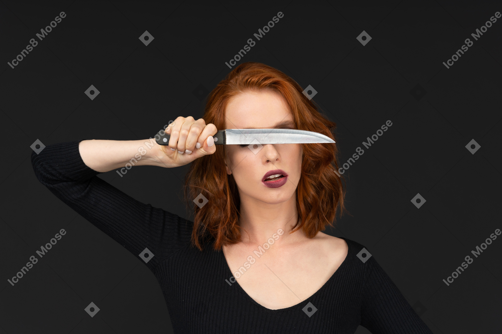 A frontal view of a sexy red haired girl covering her eyes with a knife