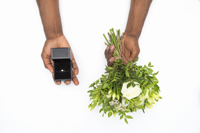 Mani maschili nere che tengono il mazzo di fiori e scatola con un anello