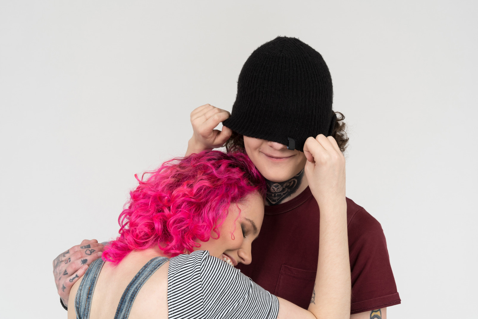 Smiling pink-haired girl puts hat oh her boyfriend