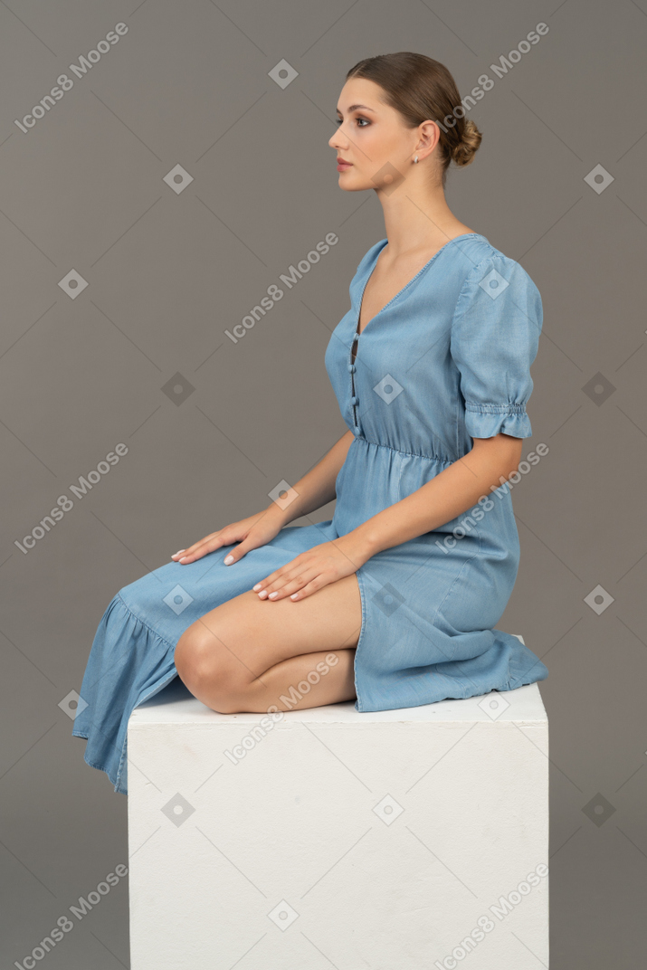 Vista laterale della giovane donna in abito blu seduto su un cubo