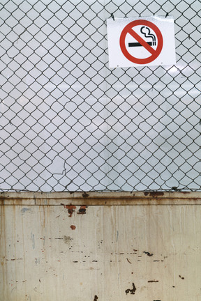 Clôture grillagée avec un bout de mur et un panneau d'interdiction de fumer