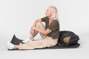 Mature female tourist sitting on tourist mat near tourist backpack