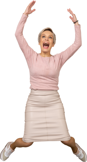 Front view of a happy woman in casual clothes jumping with raised arms