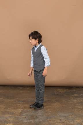 Vista lateral de un niño con traje gris mirando algo con interés