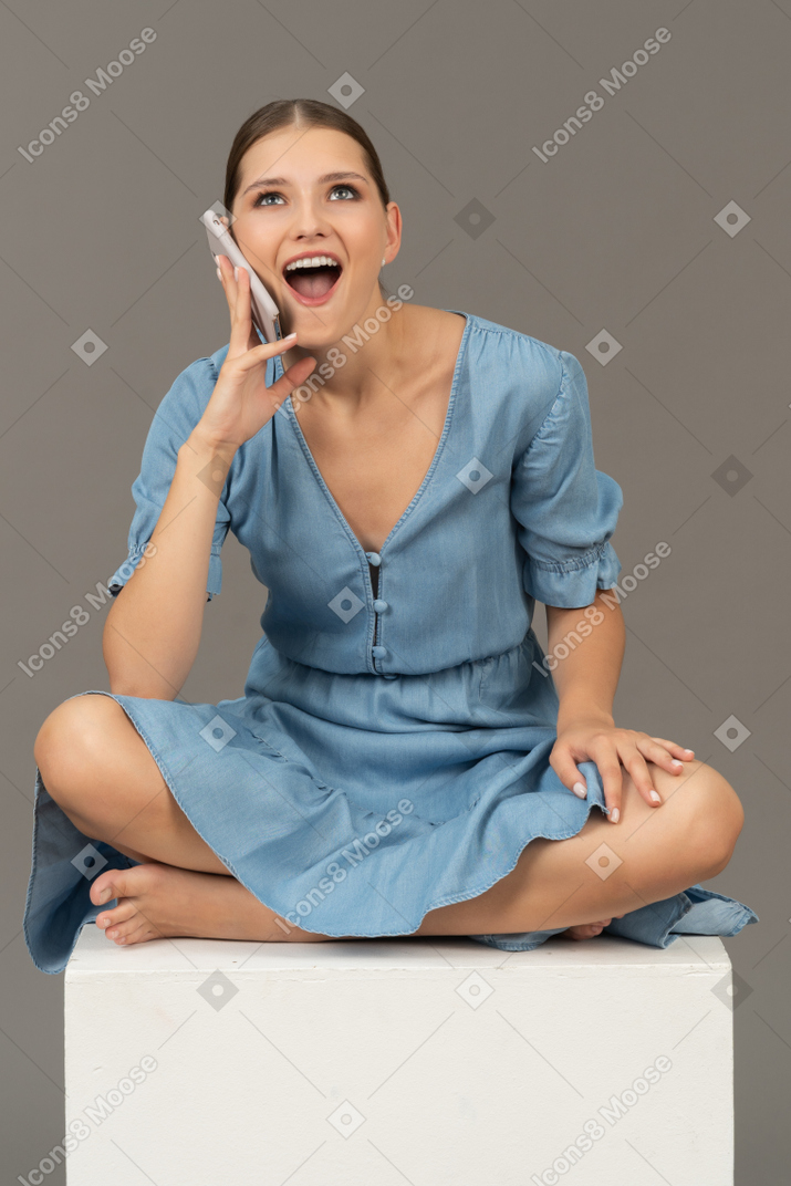 Front view of young woman sitting on a cube and talking on smartphone