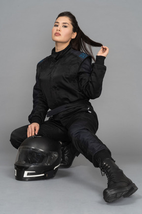 Um motociclista feminino de cócoras e tocando seus cabelos