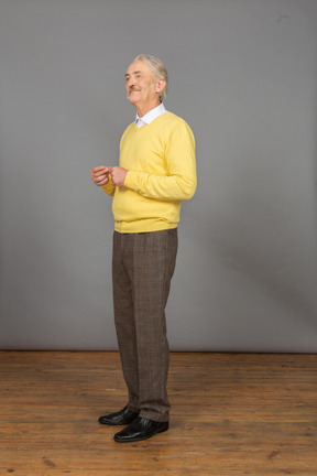 Three-quarter view of an old man in a yellow pullover putting hands together and looking aside