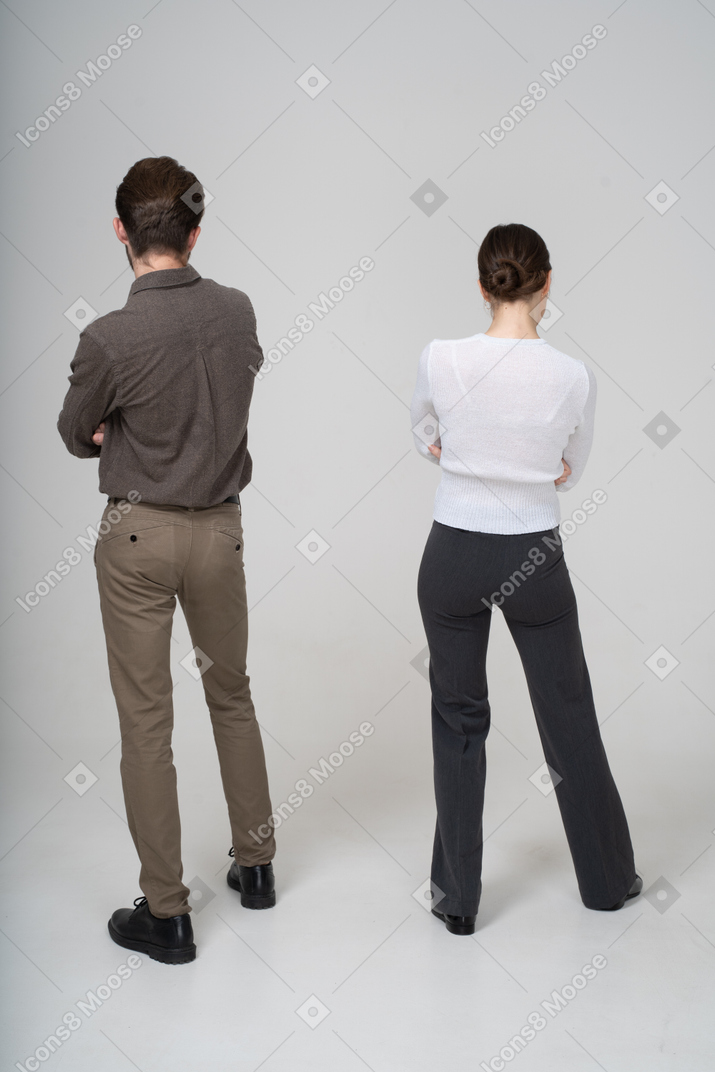一对年轻夫妇在办公室服装交叉双臂的后视图
