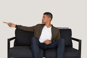 Front view of young man sitting on a sofa and passing pensil with notebook