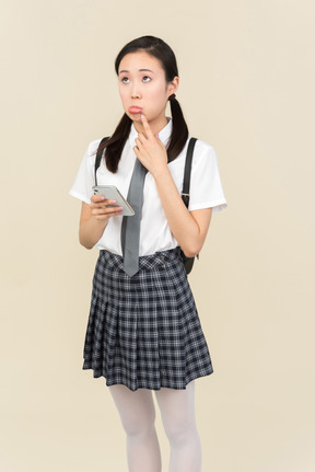 Грустно выглядящая азиатская школьница, думающая, используя телефон