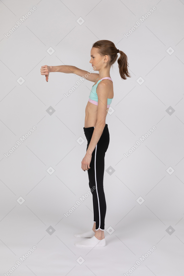 Vista laterale della ragazza teenager delusa in abiti sportivi che mostra il pollice verso il basso