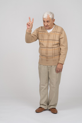 Vista frontal de un anciano con ropa informal que muestra el signo v