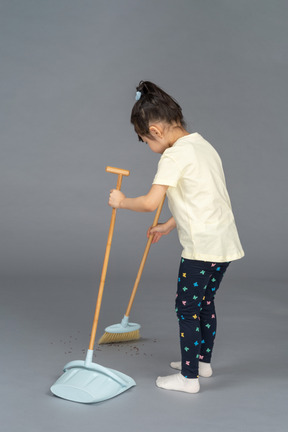 Three-quarter back view of a little girl sweeping