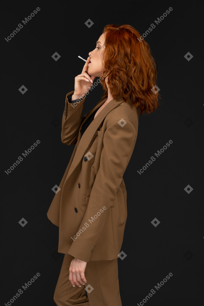 Вид сбоку на курящую женщину в коричневом костюме
