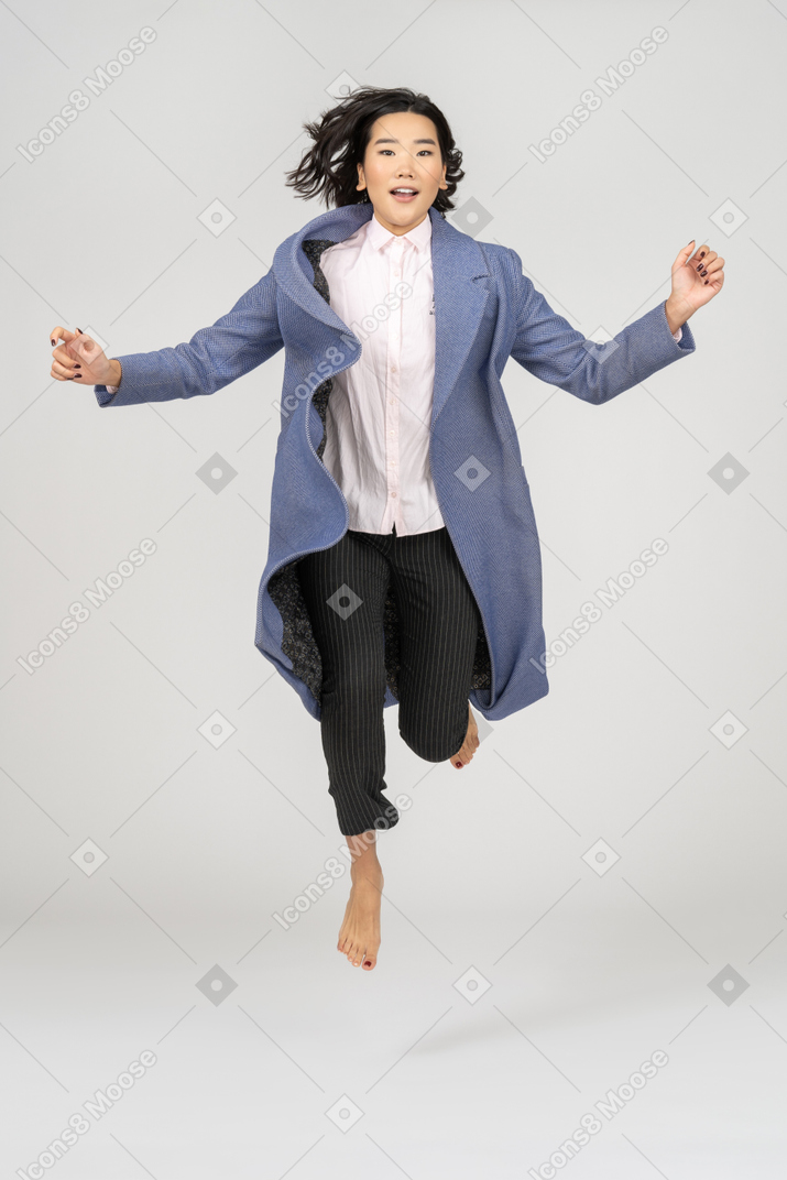 Mujer joven emocionada en abrigo saltando