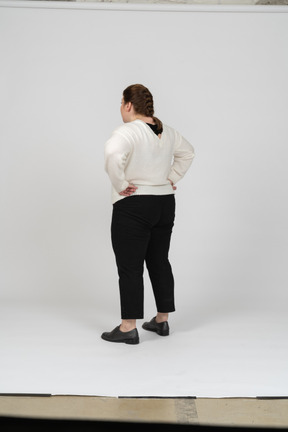 腰に手を置いて立っているカジュアルな服を着たふっくらとした女性の背面図