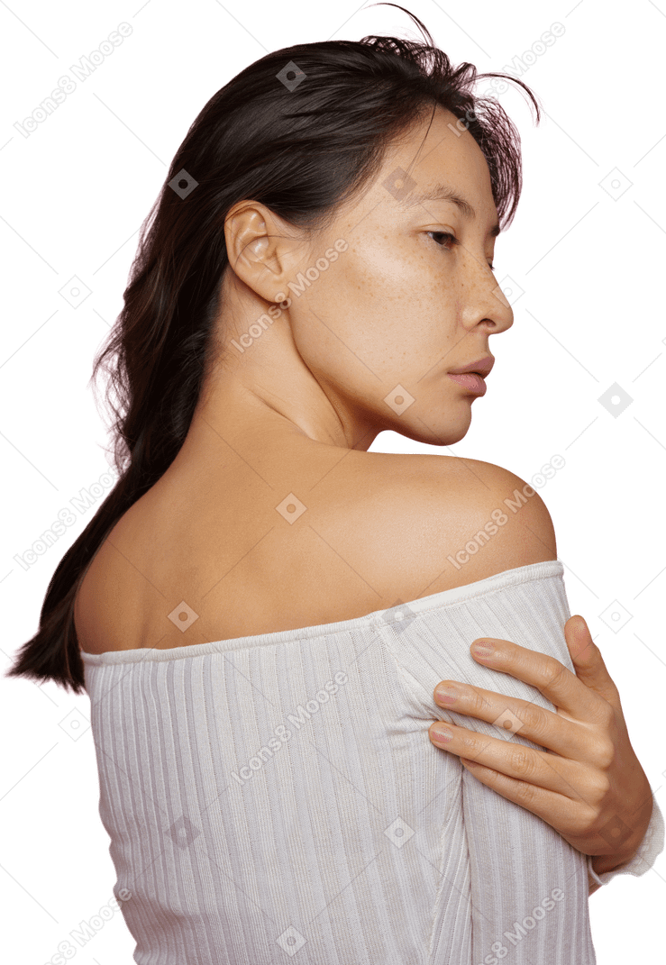 Трехчетвертный вид сзади темноволосой женщины, касающейся плеча и смотрящей в сторону