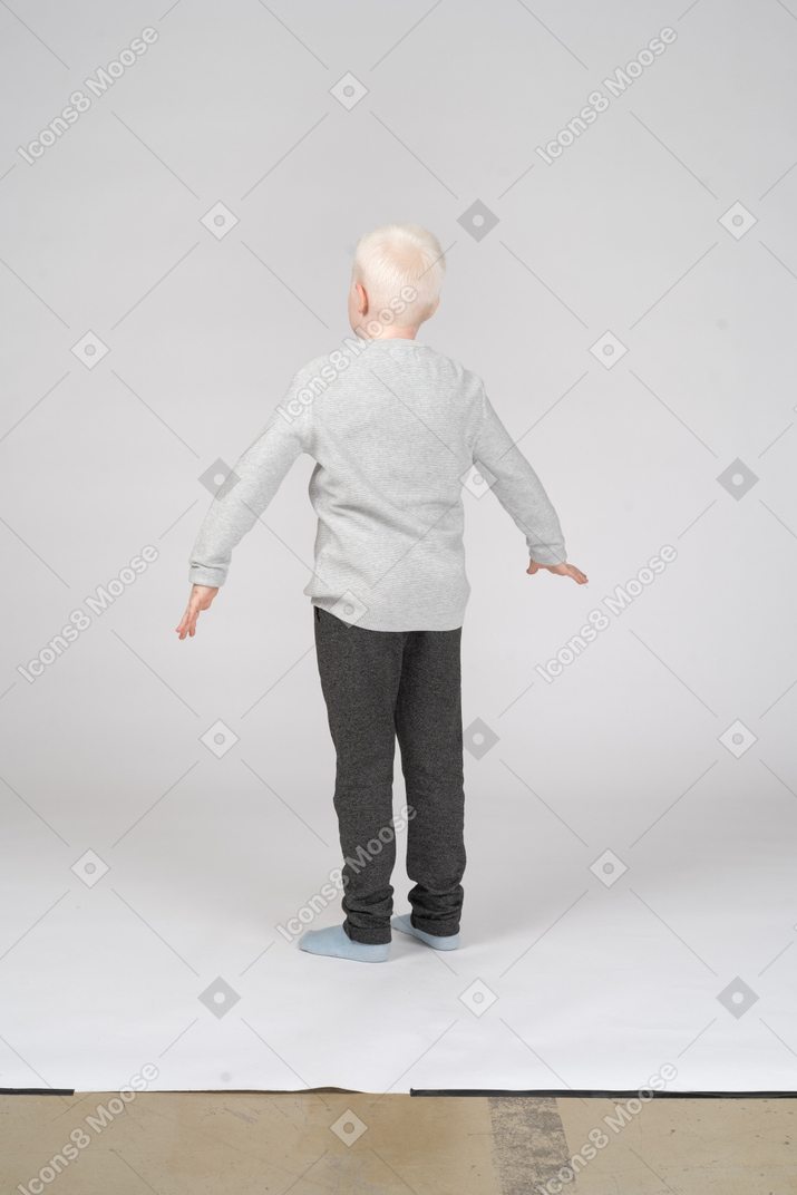Vista trasera de tres cuartos de un niño con los brazos ligeramente levantados
