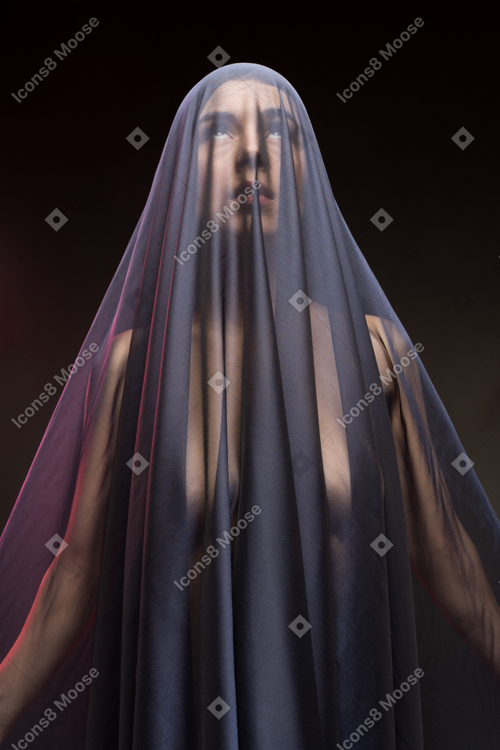 Sensual naked young woman in dark veil looking up