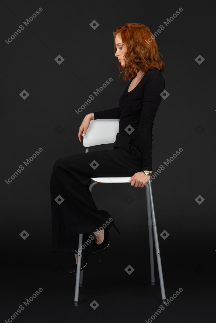 A side view of the sexy woman sitting on the tall grey chair with closed eyes