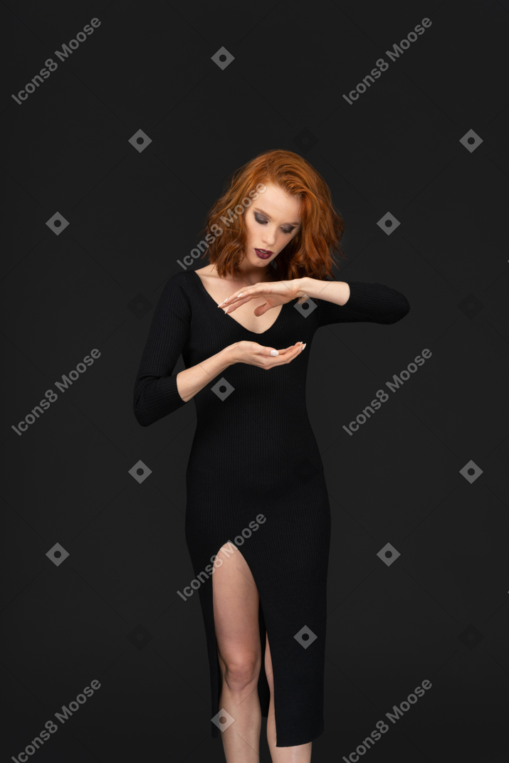 A cute young woman standing on the dark background and looking down