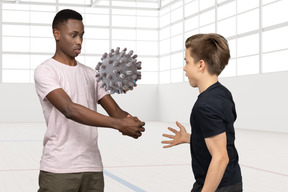 Man passing coronovirus shape ball to another man in a room