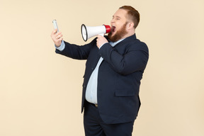 Young overweight office worker screaming at smartphone using megaphone