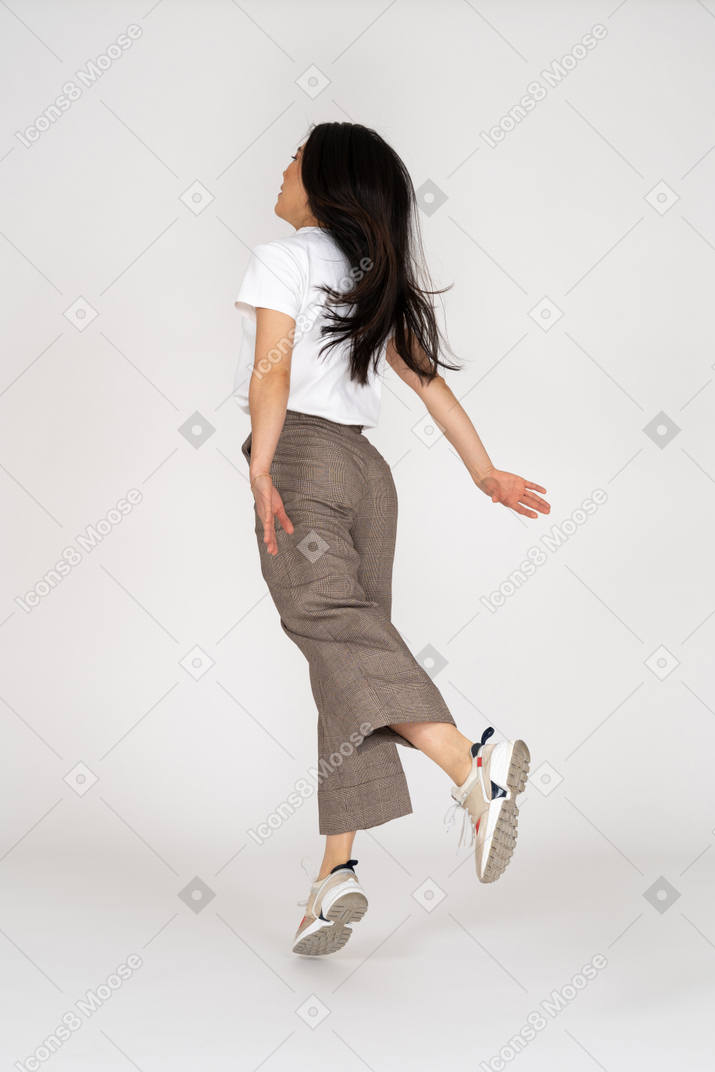 Vista traseira de três quartos de uma jovem saltitante de calça e camiseta