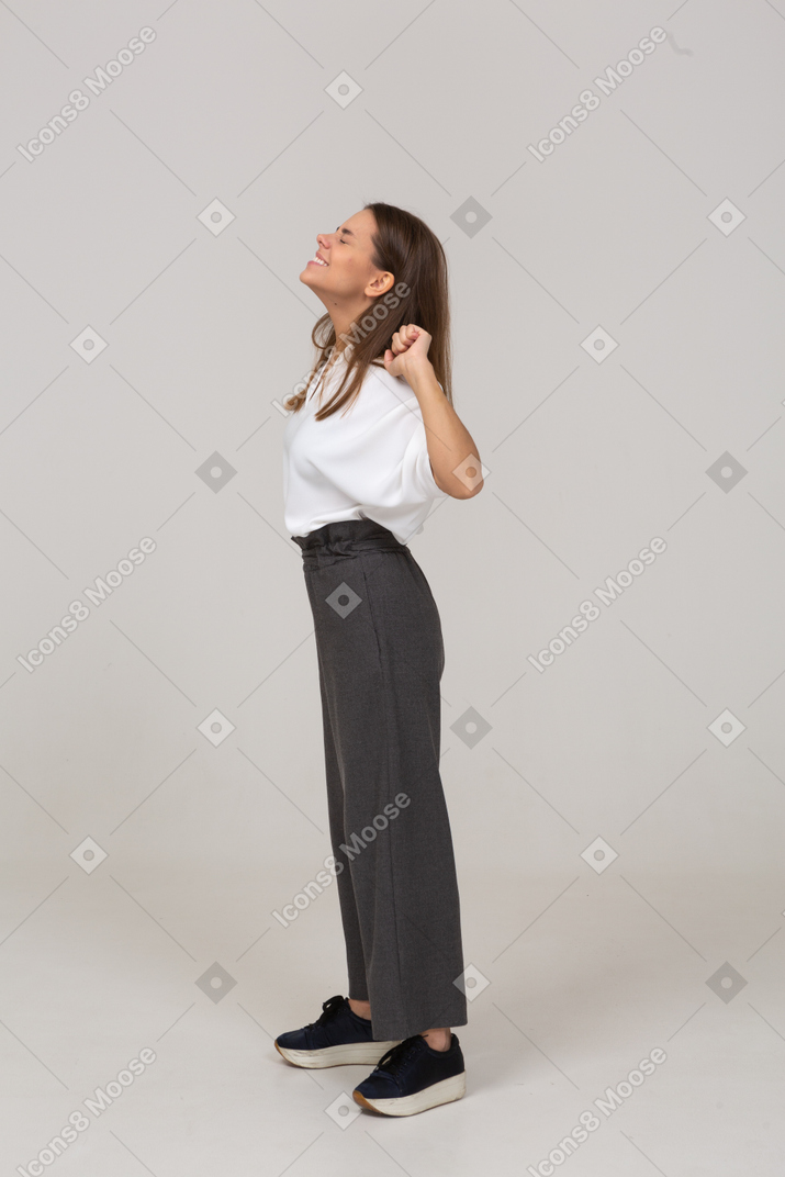 Vista lateral de una joven sonriente en ropa de oficina levantando las manos