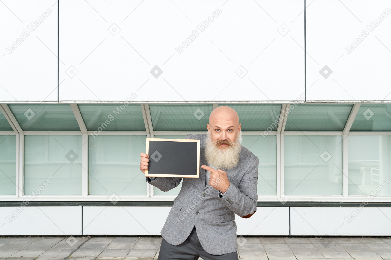 A man with a beard holding up a blank board in front of a building