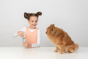 Kid girl opening a packet of dog treat for her spitz pet