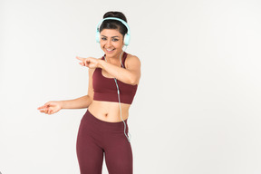 Laughing young indian woman in sporstwear listening to music in headphones