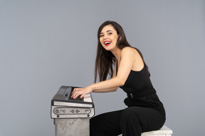 Vista lateral de uma jovem sorridente sentada de terno preto enquanto toca piano