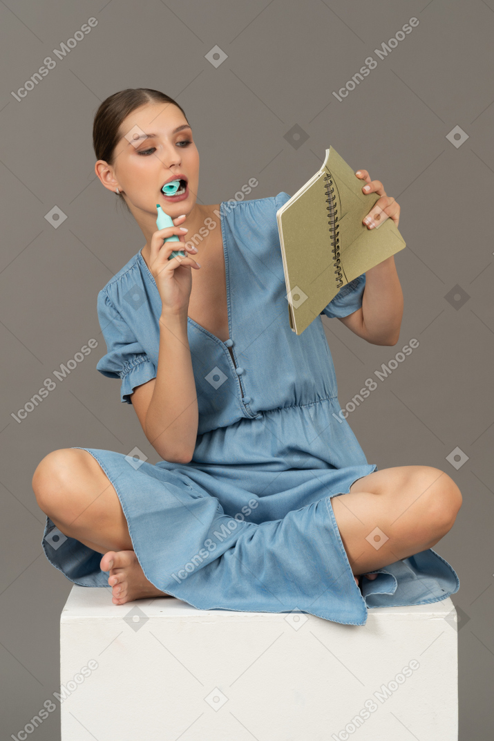Vista frontal de una joven sentada en un cubo con marcador y cuaderno