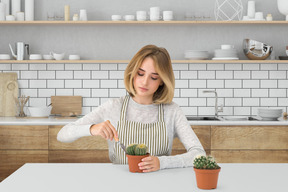 A woman sitting at a table and planting cactus with a tool
