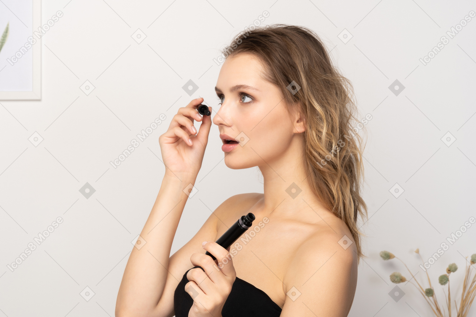 Vista de tres cuartos de una joven sorprendida vistiendo top negro aplicando rímel