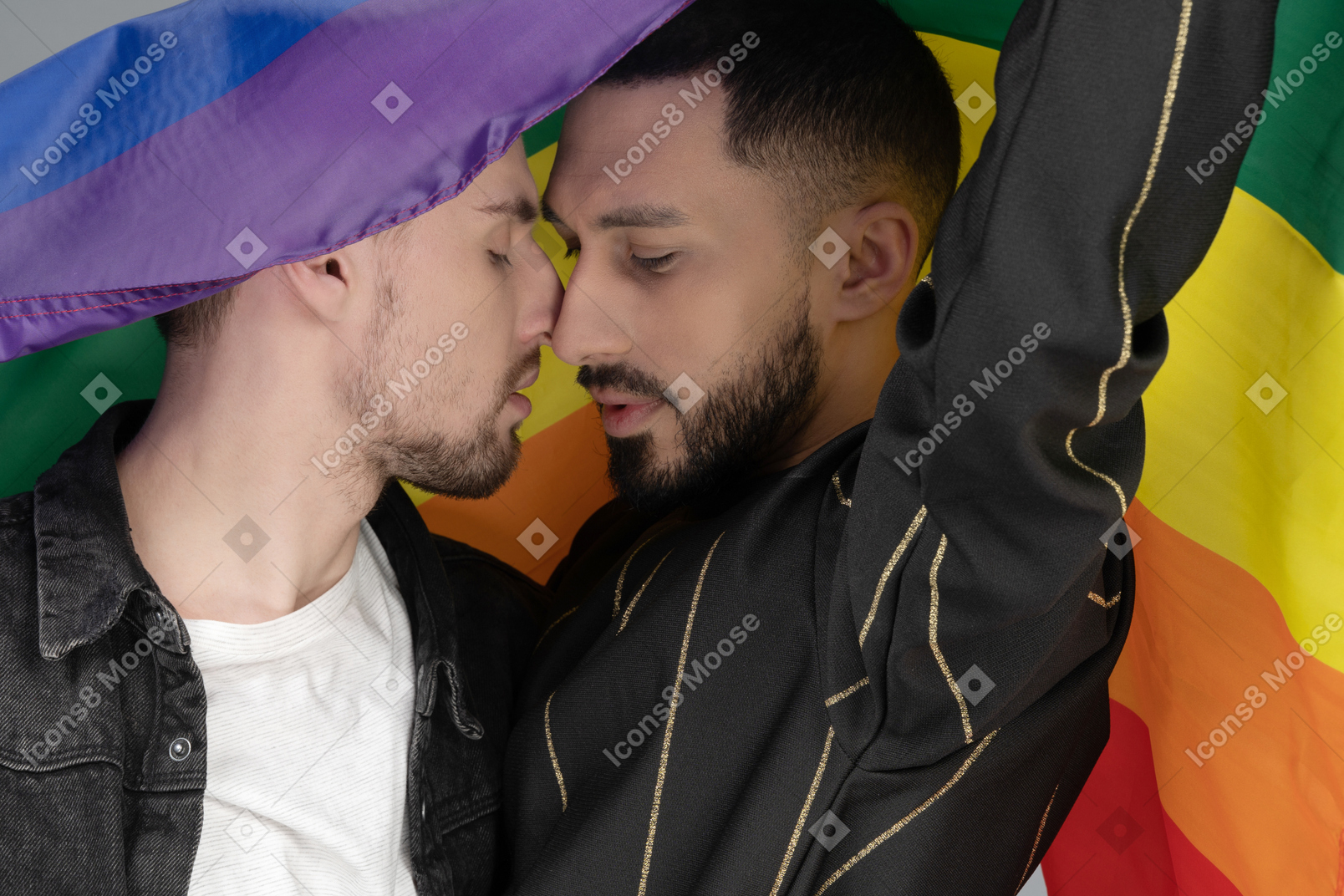 Close-up of two young men touching noses sensually under lgbt flag