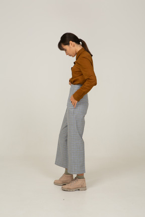 Vista laterale di una giovane donna asiatica in calzoni e camicetta che mette le mani in tasca