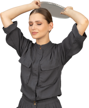 Three-quarter view of a young woman in a jumpsuit holding glass plate