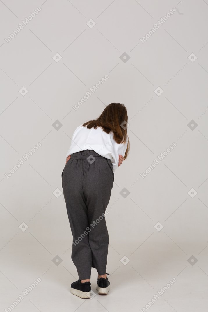 Vista posteriore di una giovane donna in abiti da ufficio con mal di stomaco che si piega