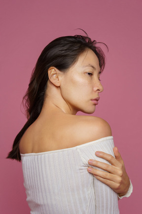 Three-quarter back view of a dark haired female touching shoulder and looking aside