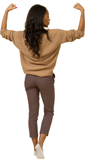 Vista posterior de una mujer joven de piel oscura levantando las manos y apretando los puños