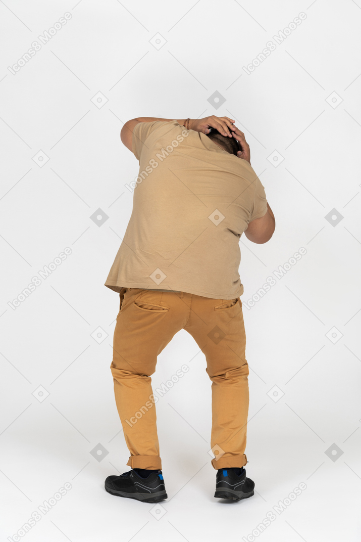 Plump man standing back to camera and covering head with both hands