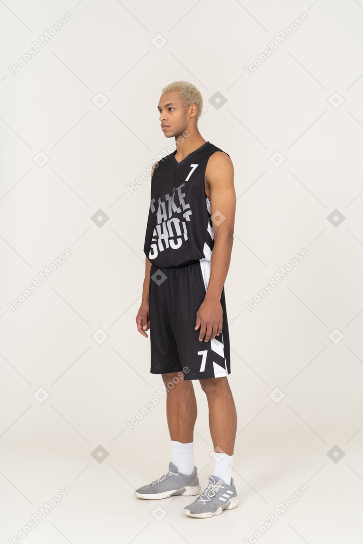 Vista di tre quarti di un giovane giocatore di basket maschile in piedi immobile e guardando da parte