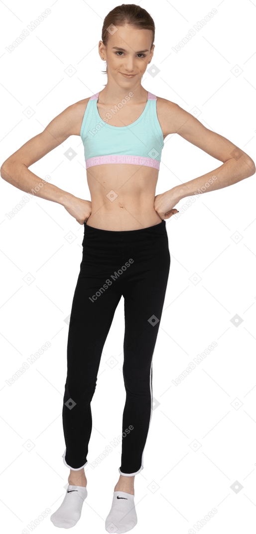 Front view of a teen girl in sportswear smiling and putting hands on hips