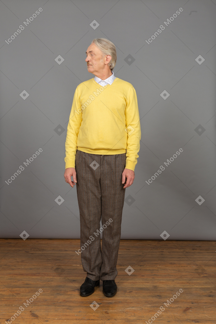 Front view of an old curious man in yellow pullover turning head and looking aside