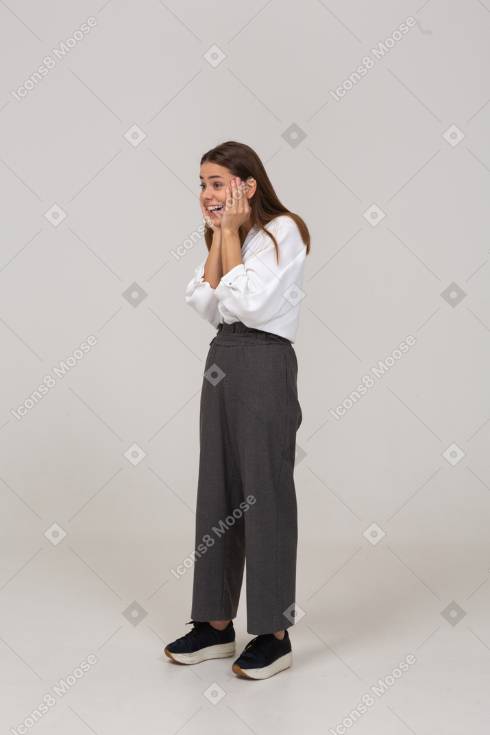 Vista de tres cuartos de una joven emocionada en ropa de oficina tocando la cara