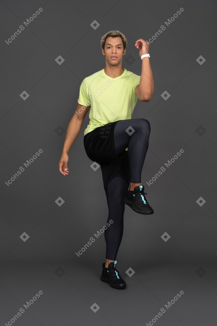 Front view of a dark-skinned young man bending knee and raising leg