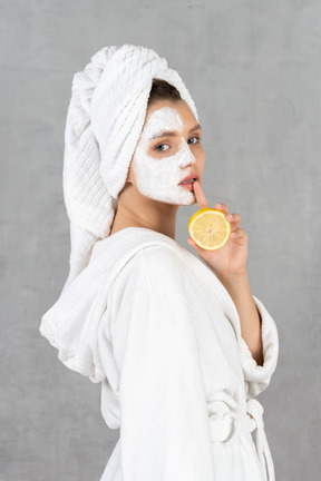 Woman in bathrobe pressing finger to lip and holding a lemon